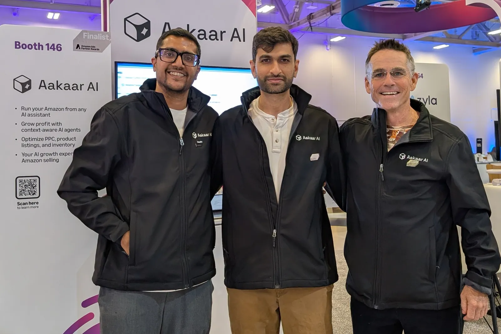 Three people in Aakaar AI jackets standing in front of the Aakaar AI booth, Booth 146, with a Finalist sign from the Amazon Ads Partner Awards